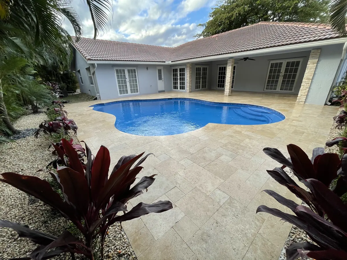 Freeform pool refilled with a new blue finish, framed by an ivory travertine deck and tropical plants